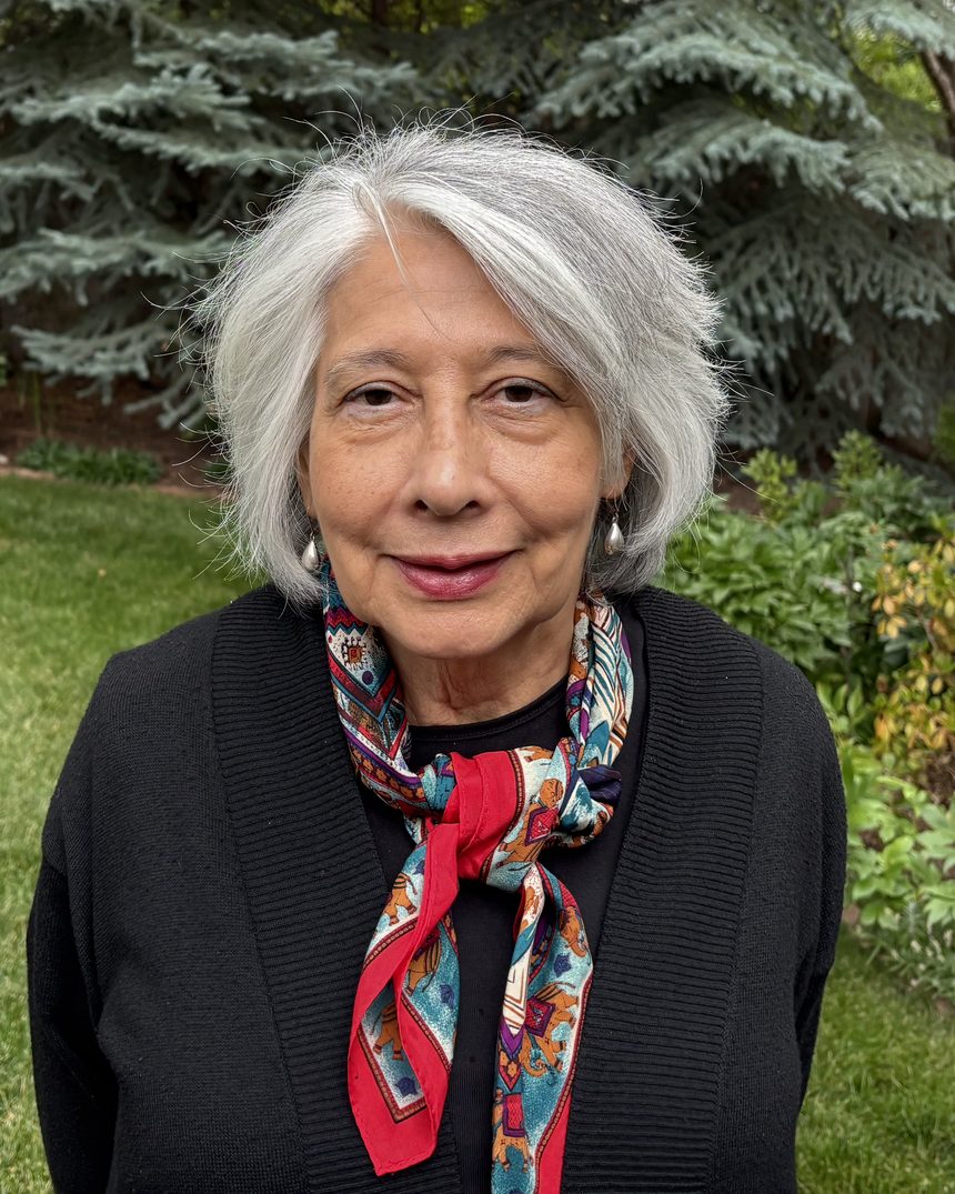 Sydnnia Wulff smiling in her garden, wearing a black cardigan and a patterned red scarf